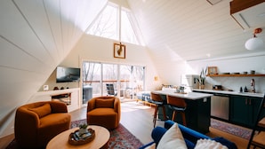 A spacious loft with a high ceiling, a dining area, kitchen, and a cozy seating area with a fireplace. - Oak Hollow | Hocking Hills, Hot Tub, Romantic (McArthur)