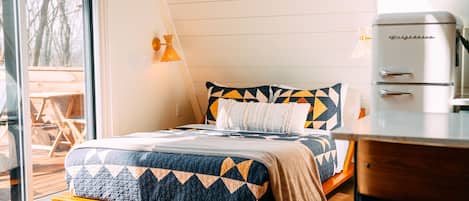 Un dormitorio con cama, un banco de madera, una mesa y un refrigerador.