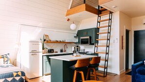 A compact living space with a kitchenette, a bed with patterned bedding, and a blue chair. - Oak Hollow | Hocking Hills, Hot Tub, Romantic (McArthur)