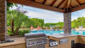 Eine Außenküche mit Grill, Spüle und Gasherd mit Blick auf einen Swimmingpool.