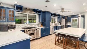 A modern kitchen with blue cabinets, stainless steel appliances, and a large island with stools. - Urban-Oasis with Resort Style Pool (Phoenix)