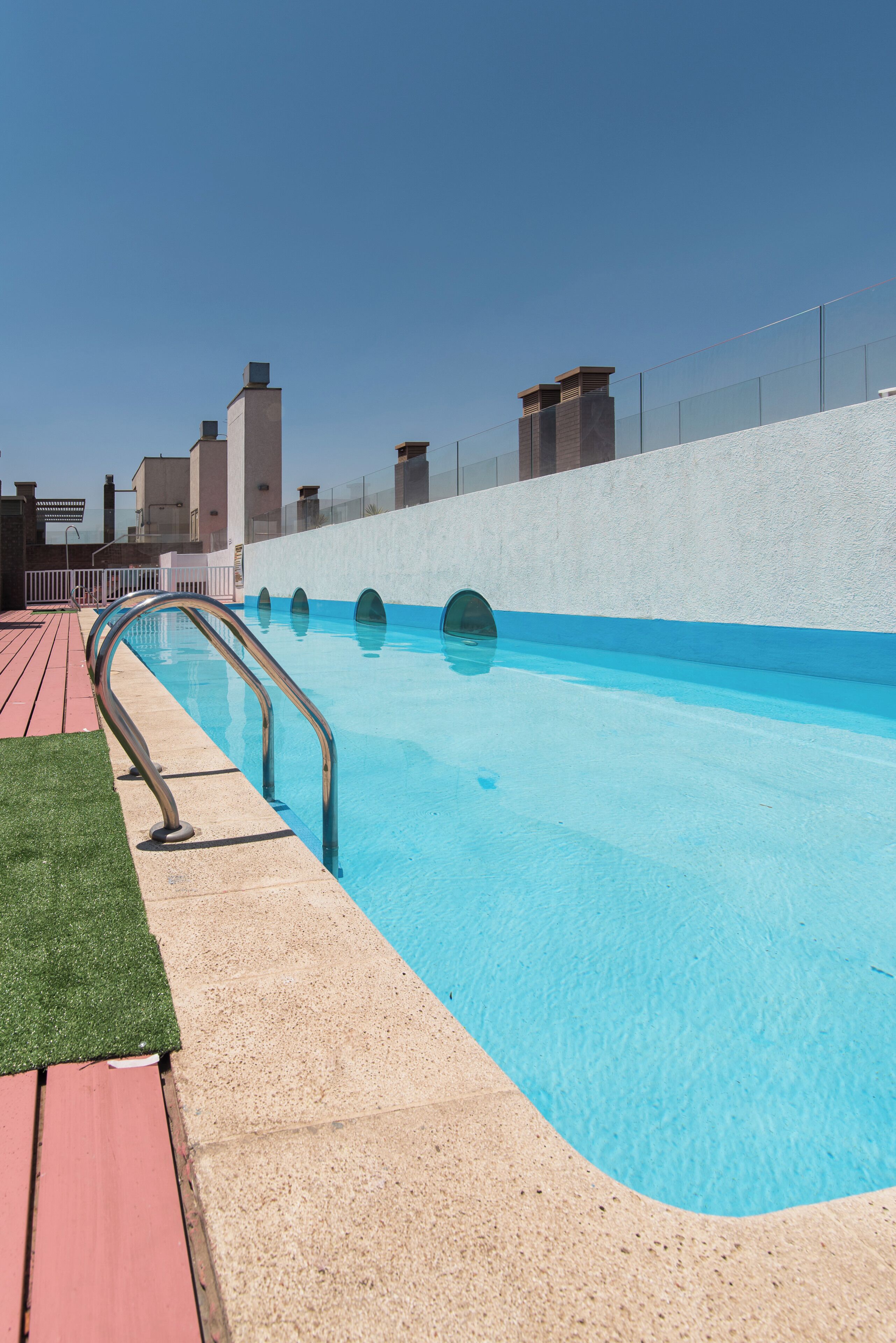 A swimming pool with a metal ladder, a red deck, and a white wall with a fence.