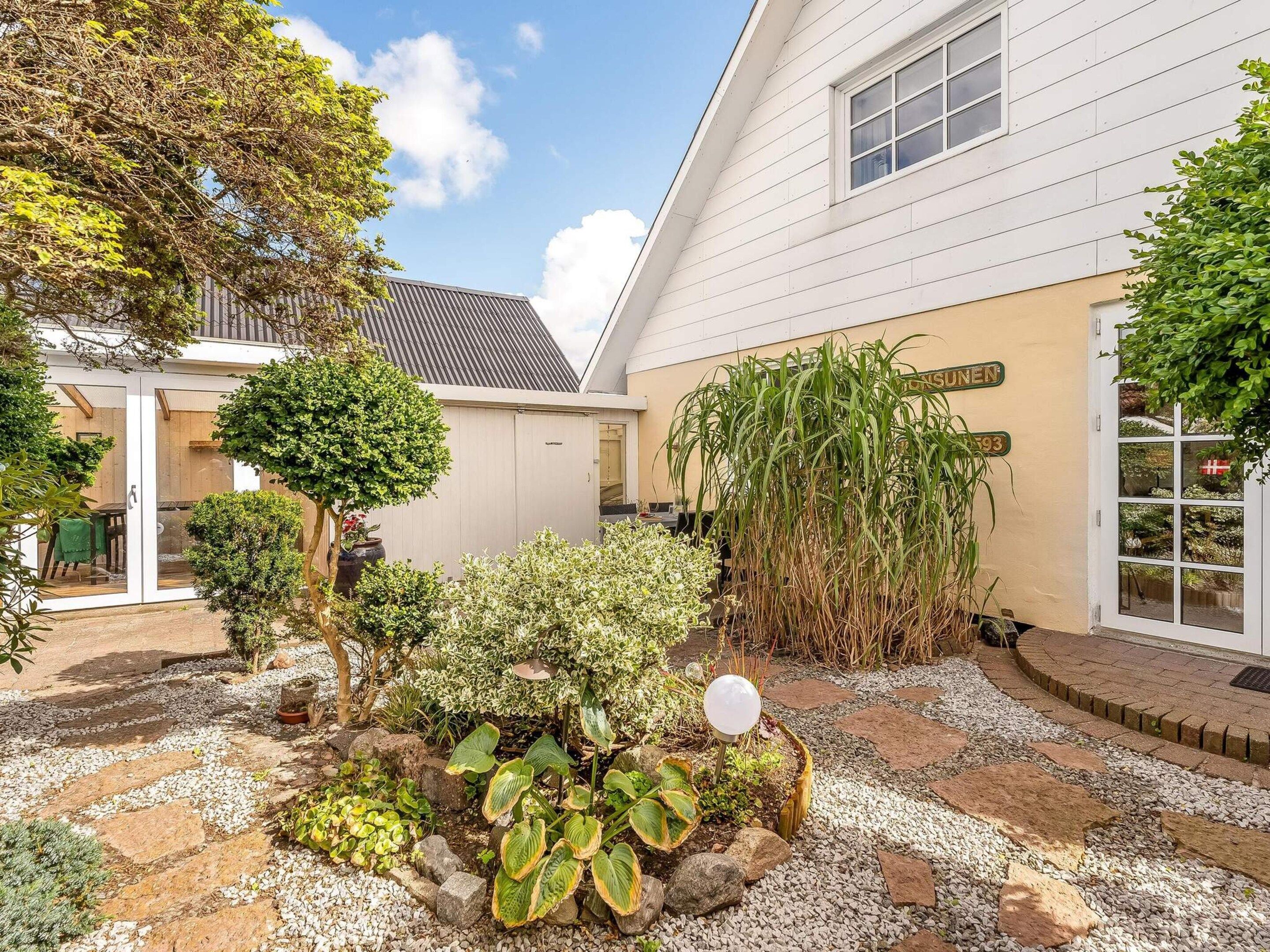 A residential property with a white exterior, a gravel garden, and a variety of plants.