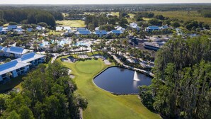 Eine Vogelperspektive eines Golfplatzes mit Teich, umgeben von Gebäuden mit blauen Dächern und dichter Vegetation.