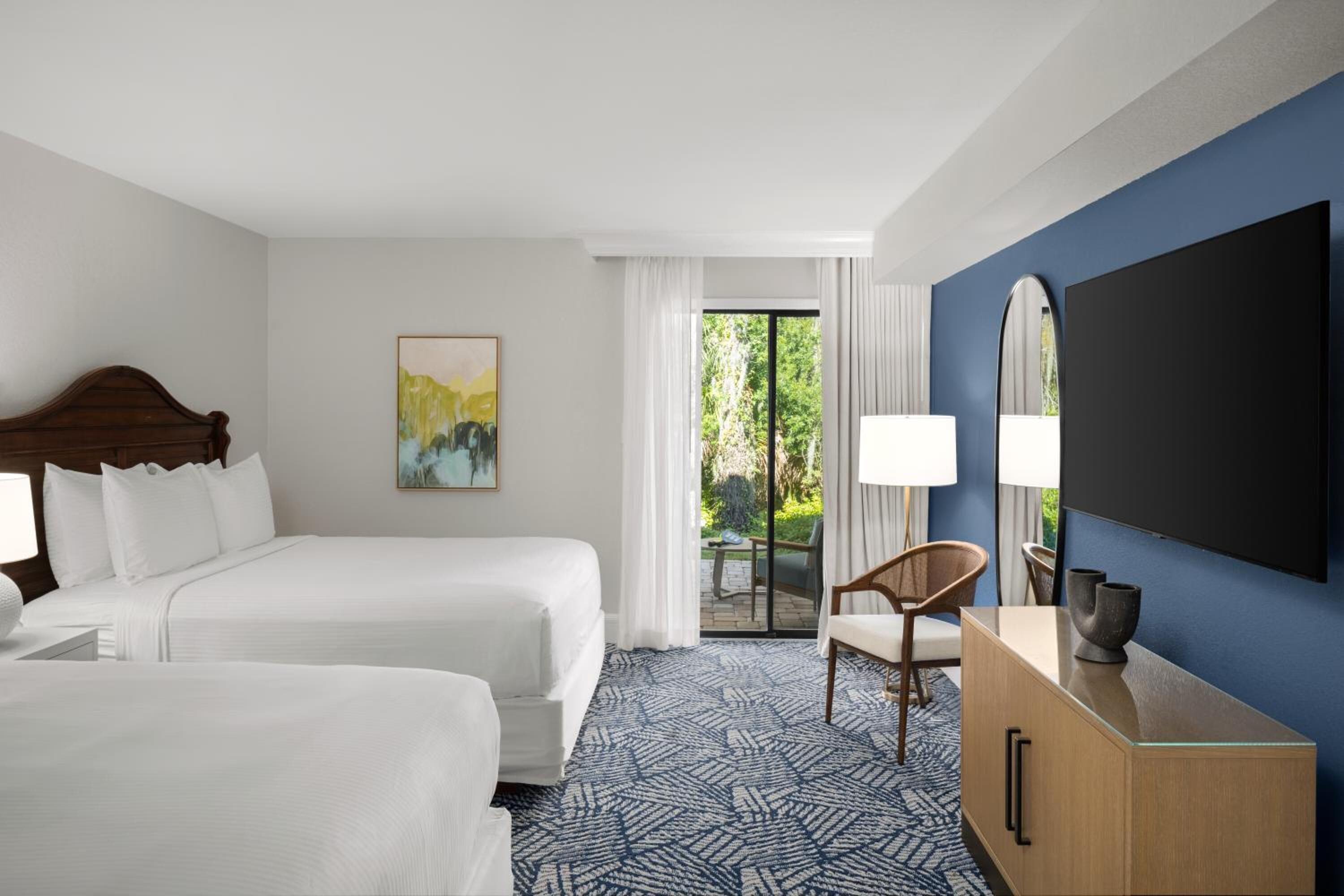 A hotel room with two beds, a large mirror, a flat-screen TV, a wooden dresser, and a view of the outdoors.