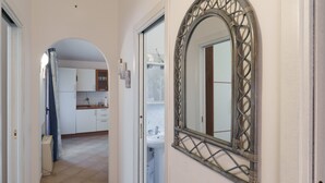 Un pasillo con un espejo, una puerta y vista hacia una cocina.