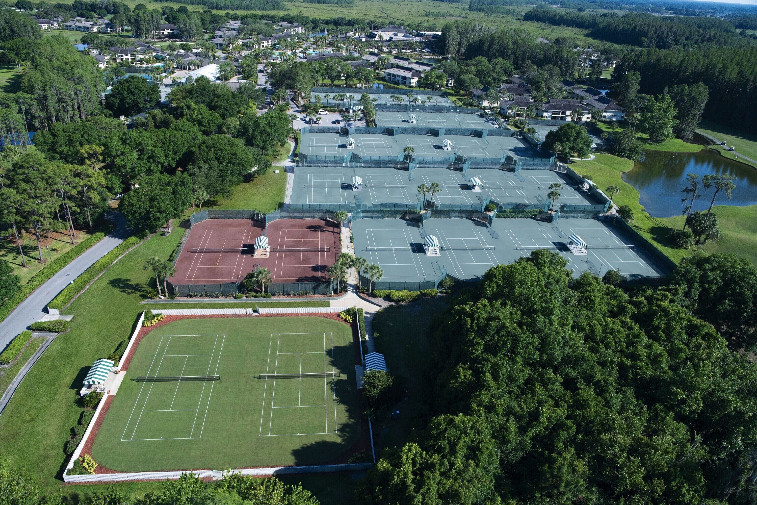 Vista aérea de una zona residencial con varias canchas de tenis, un amplio campo verde y un lago.