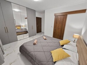 A bedroom with a bed, a wardrobe, a mirror, and a door. - National Park views Apartment Terrace 2 bedroom 2 bathroom (San Pawl il-Baħar)