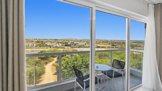 Un balcón con mesa y sillas, y una vista despejada de un paisaje con edificios y vegetación.