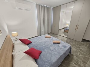 A bedroom with a bed, pillows, a lamp, a wardrobe, and a mirror. - 5th Floor enjoying open views of the National  Park, 2 bedroom 2 Bathroom (San Pawl il-Baħar)
