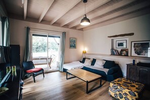 Ein gemütliches Wohnzimmer mit einer Couch, einem Couchtisch und einem Fernseher. Eine Schiebetür führt zu einem Außenbereich.