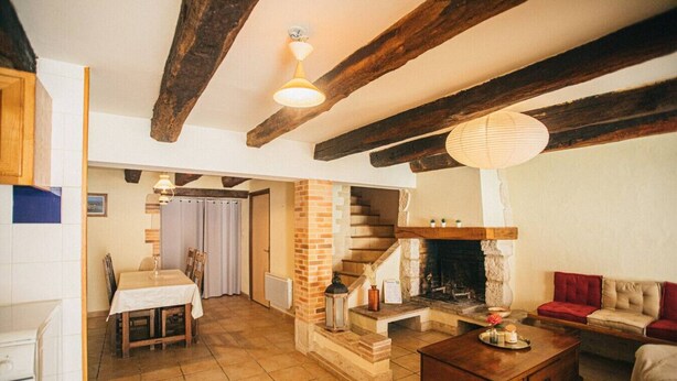 Ein rustikales Interieur mit freiliegenden Holzbalken, einem Kamin, einem Essbereich und einem Wohnzimmer mit einer Couch.
