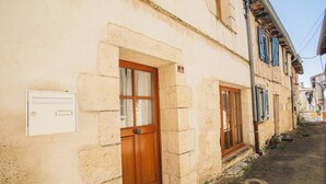 Eine enge Straße mit traditionellen Steinbauten, Holztüren und einem Verteilerkasten an der Wand.
