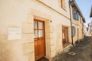 Une rue étroite bordée de bâtiments traditionnels en pierre, de portes en bois et d’une boîte de raccordement électrique fixée au mur.