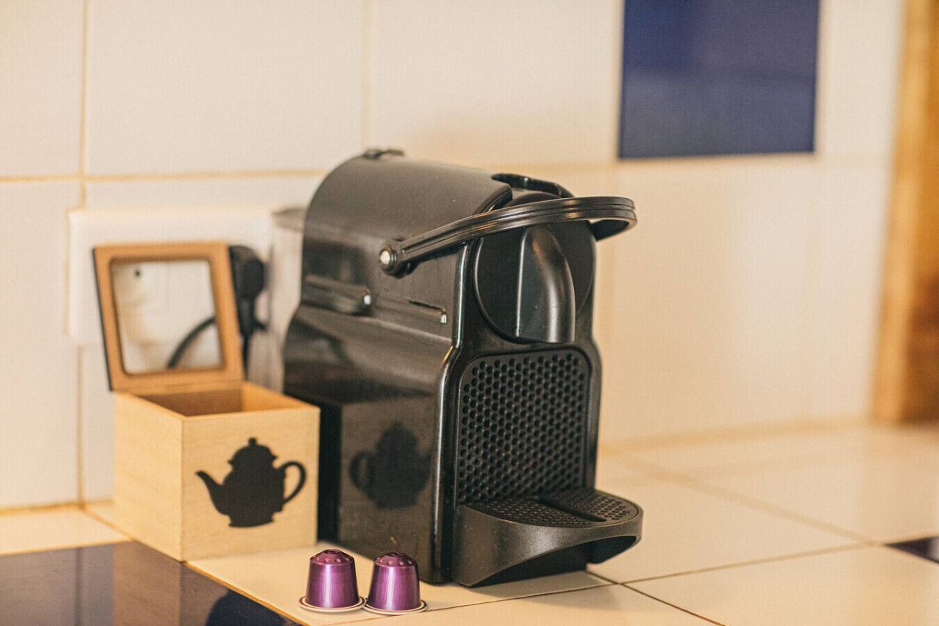 Une cuisine équipée d’une machine à café, d’une boîte en bois contenant une théière et de deux tasses violettes.