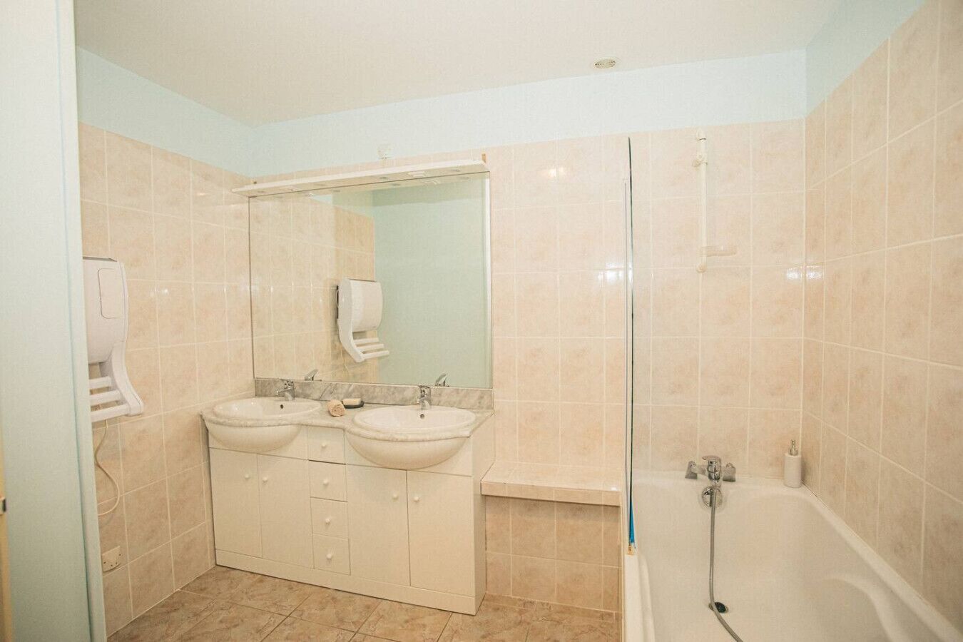 Un baño con dos lavamanos, un espejo, cabina de ducha de vidrio y un inodoro.