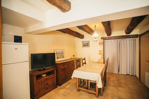 Eine Küche mit Fernseher, Holzschränken, einem Esstisch und einer Decke mit sichtbaren Balken.