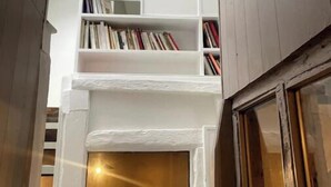 A narrow hallway with a white bookshelf, a wooden door, and a window with a view of the outside.