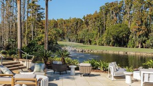 A patio with outdoor furniture, a view of a golf course, and tall trees. - 2BR Family | Saddlebrook Resort | Super Pool, Nature Trails, Car-Free Village (Wesley Chapel)