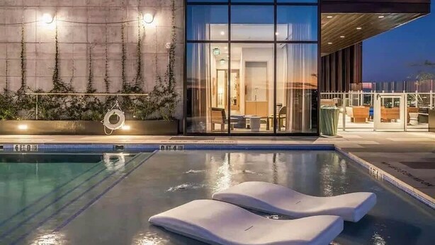 A modern building with a glass facade, a pool with lounge chairs, and a view of the interior. - Luxury Downtown Austin Condo Near Rainey Street (Austin)
