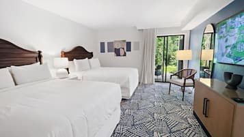A hotel room with two beds, a desk with a chair, a TV, and a large window with a view of greenery.