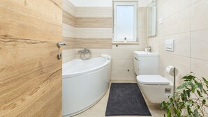 A modern bathroom with a bathtub, toilet, and sink, featuring wooden paneling and a small window. - Charming apartment in fabulous Pula with refreshing AC (Pula)
