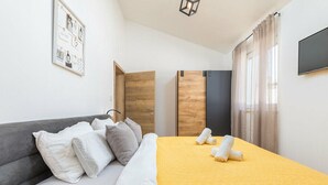 A hotel room with a bed, pillows, a yellow blanket, a grey sofa, a wooden wardrobe, a TV, and a framed picture on the wall. - Charming apartment in fabulous Pula with refreshing AC (Pula)