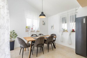 A dining area with a wooden table, grey upholstered chairs, a black pendant light, and a black refrigerator. - Charming apartment in fabulous Pula with refreshing AC (Pula)