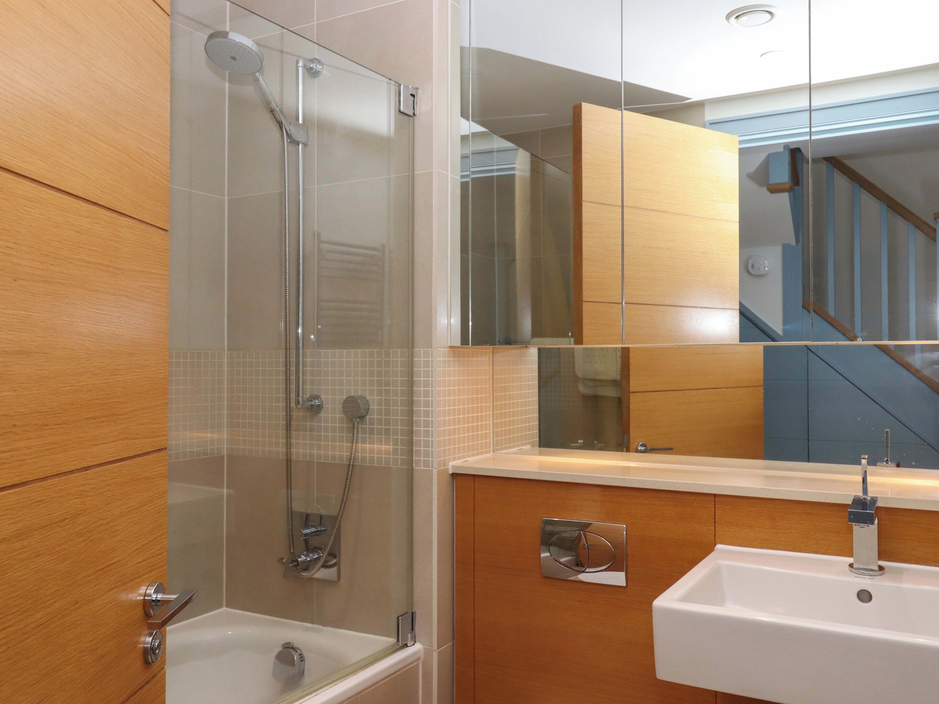 Une salle de bain moderne avec une douche à parois de verre, un lavabo blanc et un meuble-lavabo en bois.