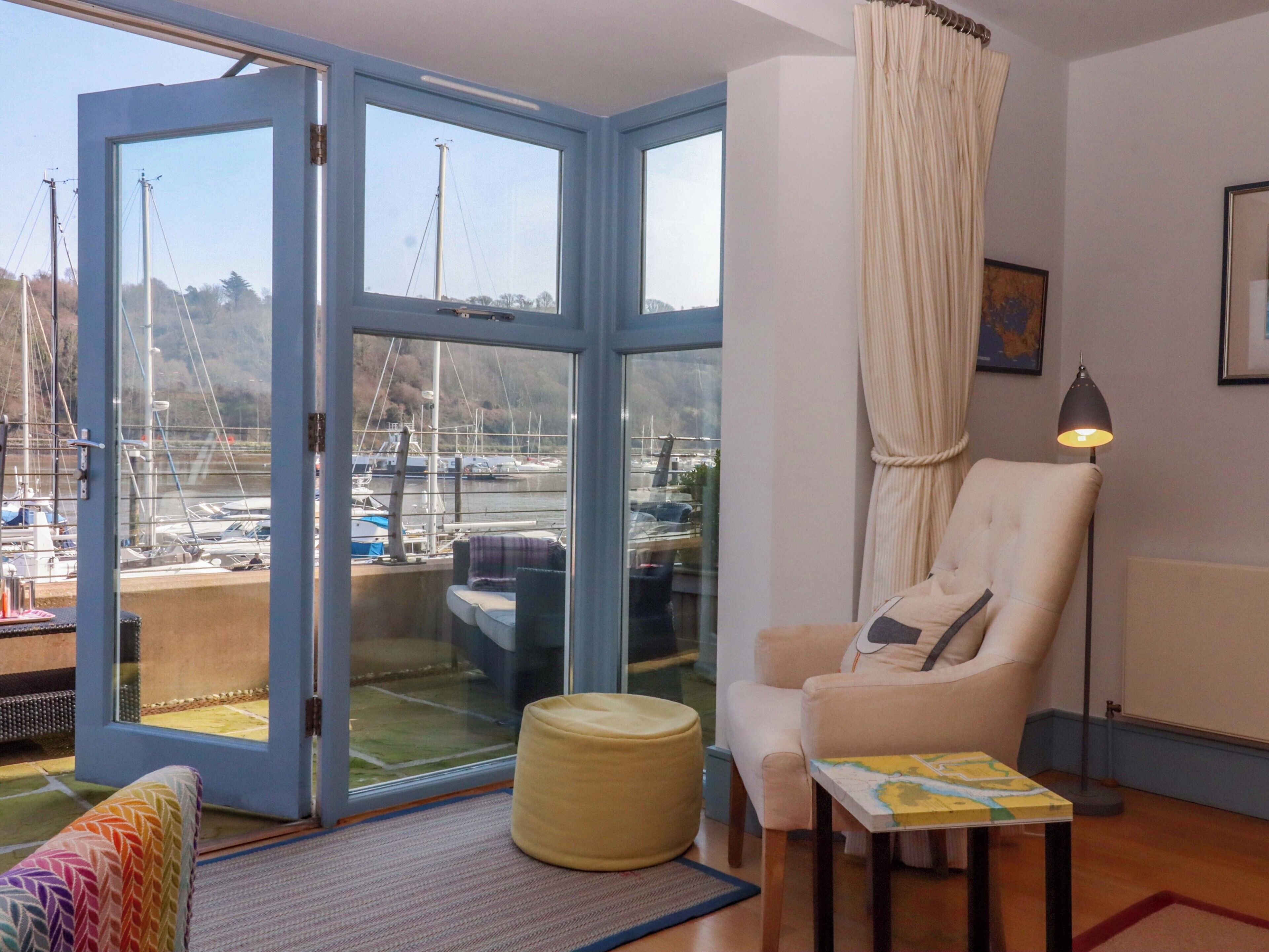 Quarto com uma grande porta de vidro deslizante para vista do porto, poltrona estofada, pequena mesa com um mapa e luminária de chão.