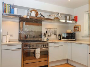 Een moderne keuken met een inbouwoven, een magnetron en diverse keukengerei dat aan de muur hangt.