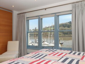 Een slaapkamer met een groot raam, een bed, een stoel en uitzicht op boten op een rivier.
