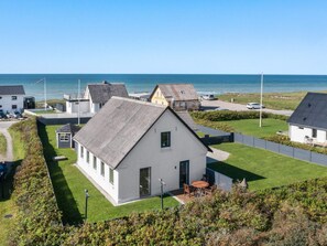 Un quartier résidentiel situé sur la côte, avec des maisons, une pelouse verdoyante et une vue dégagée sur la mer.