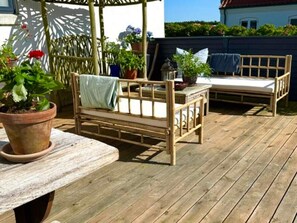 Une terrasse en bois avec un banc en bois et une petite table, le tout entouré de plantes en pot.