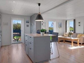 Eine geräumige Küche mit Kochinsel, eine Essecke mit Holztisch und ein Wohnzimmer mit Sofa.