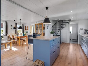 Eine geräumige Küche mit einer zentralen Kochinsel, Holzboden und einer Treppe, die in ein Obergeschoss führt.