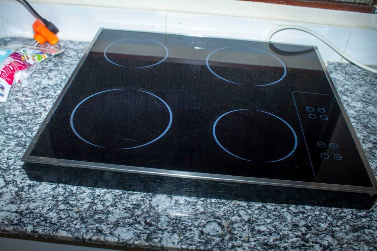 A black induction cooktop with four circular heating zones and a control panel on a granite countertop.