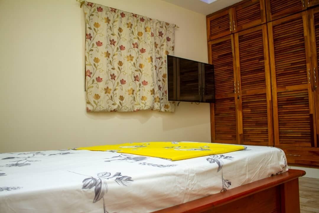A bedroom with a bed, a television mounted on the wall, and wooden wardrobes.