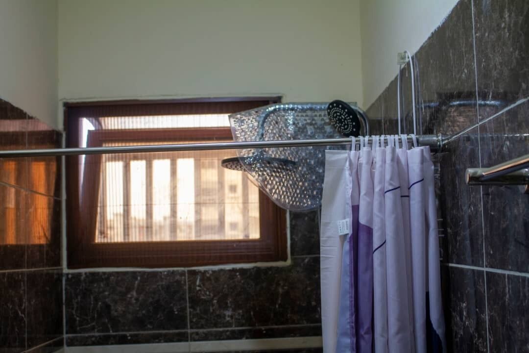 A bathroom with a shower, a window with blinds, and a towel rack.