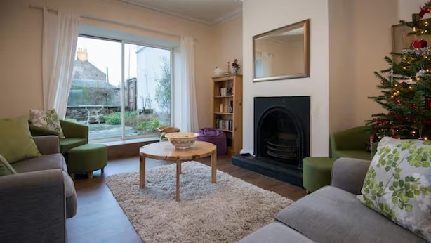A living room with a fireplace, green sofas, a coffee table, and a Christmas tree. - Near Beach - Pets - Bbq - Fireplace - Sleeps 10 (Leven)