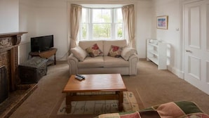 A living room with a sofa, a coffee table, a fireplace, a television, and a window with curtains. - Near Beach - Pets - Bbq - Fireplace - Sleeps 10 (Leven)