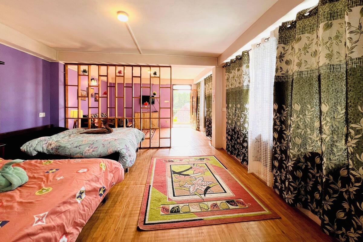 A bedroom with two beds, a wooden floor, purple walls, a decorative partition, and a view through a door.
