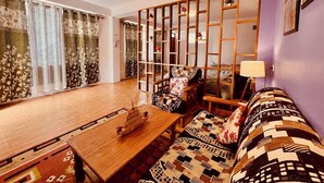 A room with a wooden table, a patterned sofa, a decorative partition, and a window with curtains.
