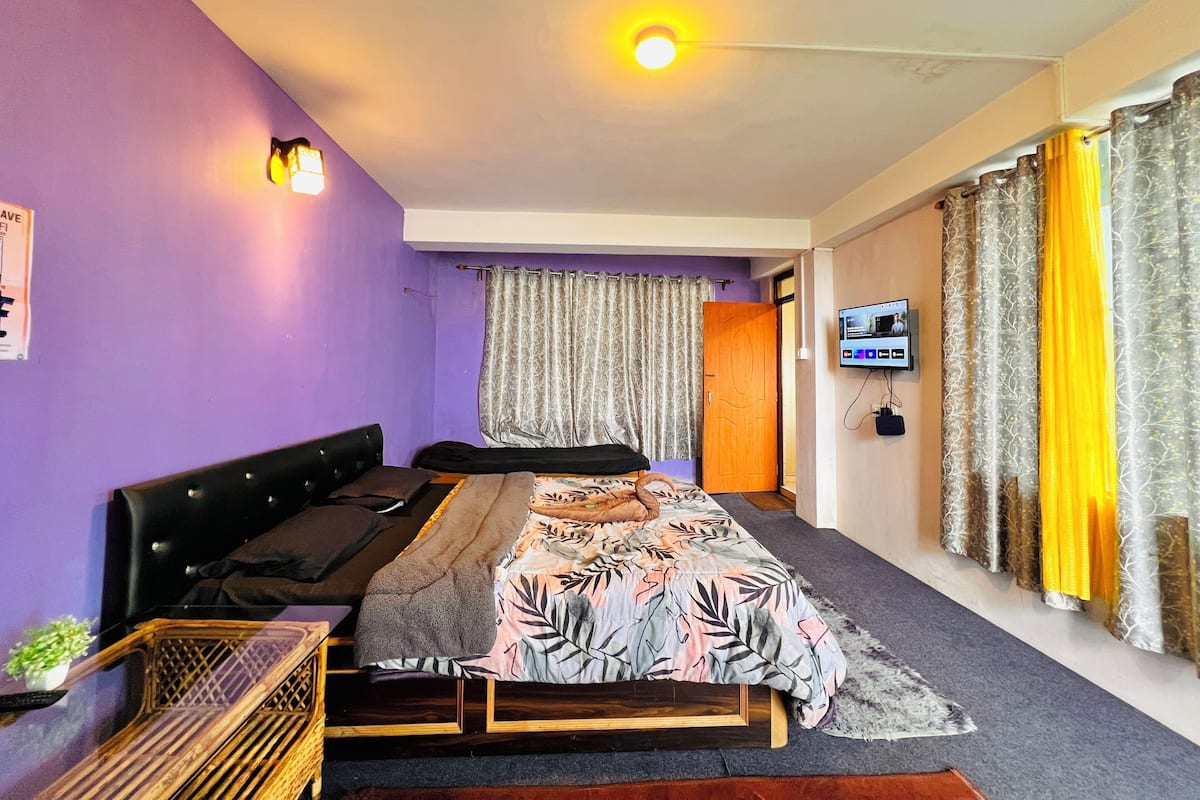 A bedroom with a bed, a television, curtains, and a wall-mounted light fixture.