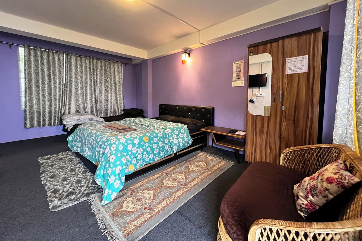 A bedroom with a bed, a chair, a bedside table, a rug, a curtain, and a wall-mounted TV.