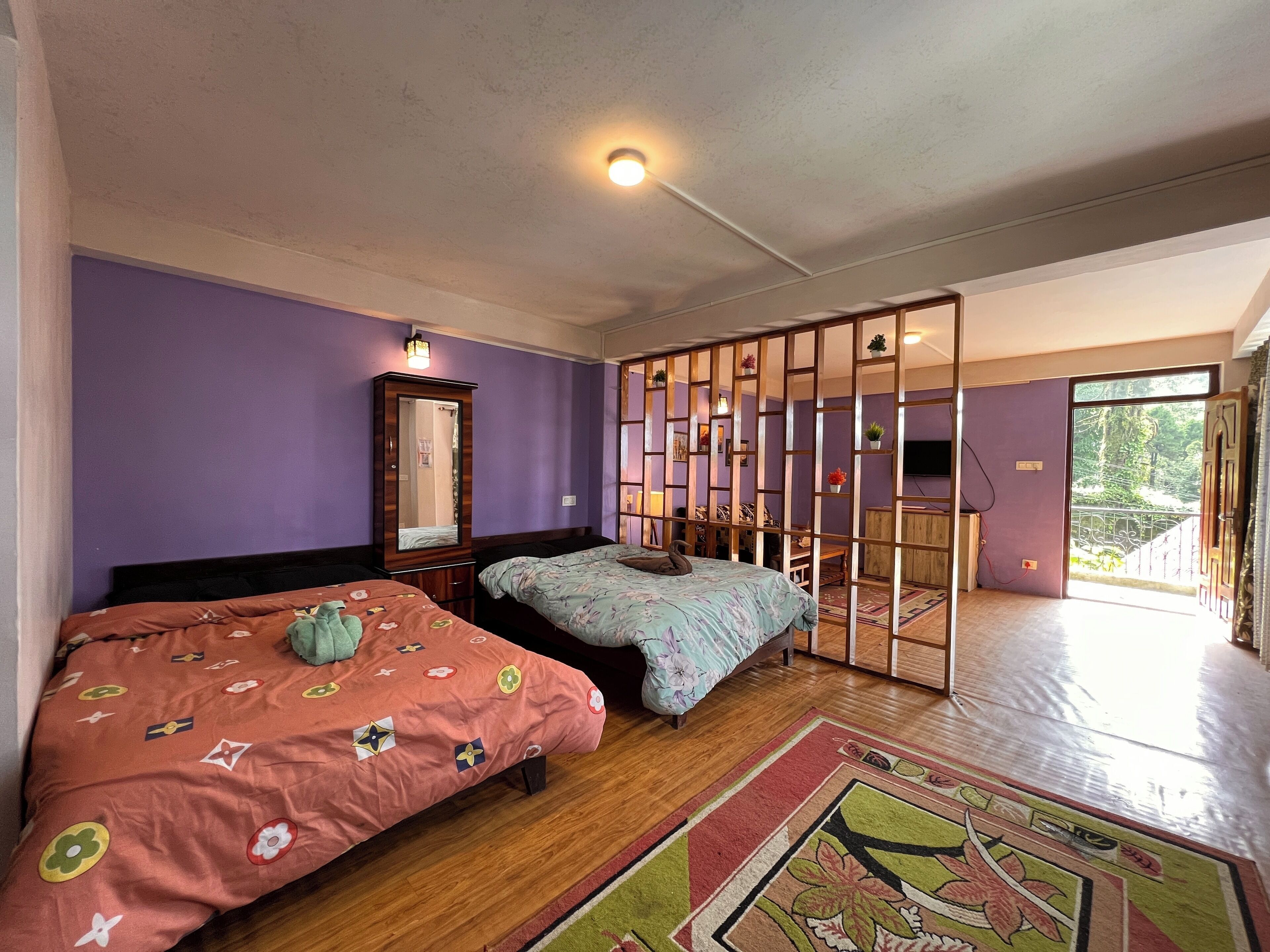 A bedroom with two beds, a wardrobe, a mirror, a partition, and a view of the outdoors.