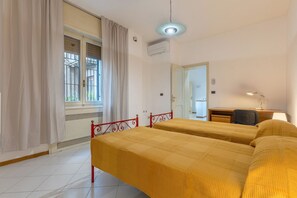 Una habitación con dos camas, un escritorio, una silla, una lámpara y una ventana con cortinas.