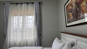 A hotel room with a large bed, a window with sheer curtains, and a framed picture on the wall.
