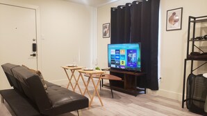 Ein Wohnzimmer mit einer Couch, einem kleinen Tisch, einem Fernseher und einem Kleiderständer.