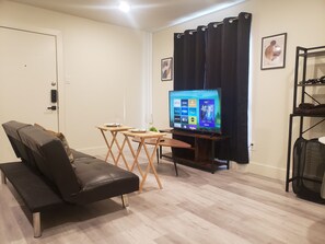A living room with a sofa, a small table, a TV, and a coat rack. - Welcome To East Dallas! King Bed! Near It All (Dallas)